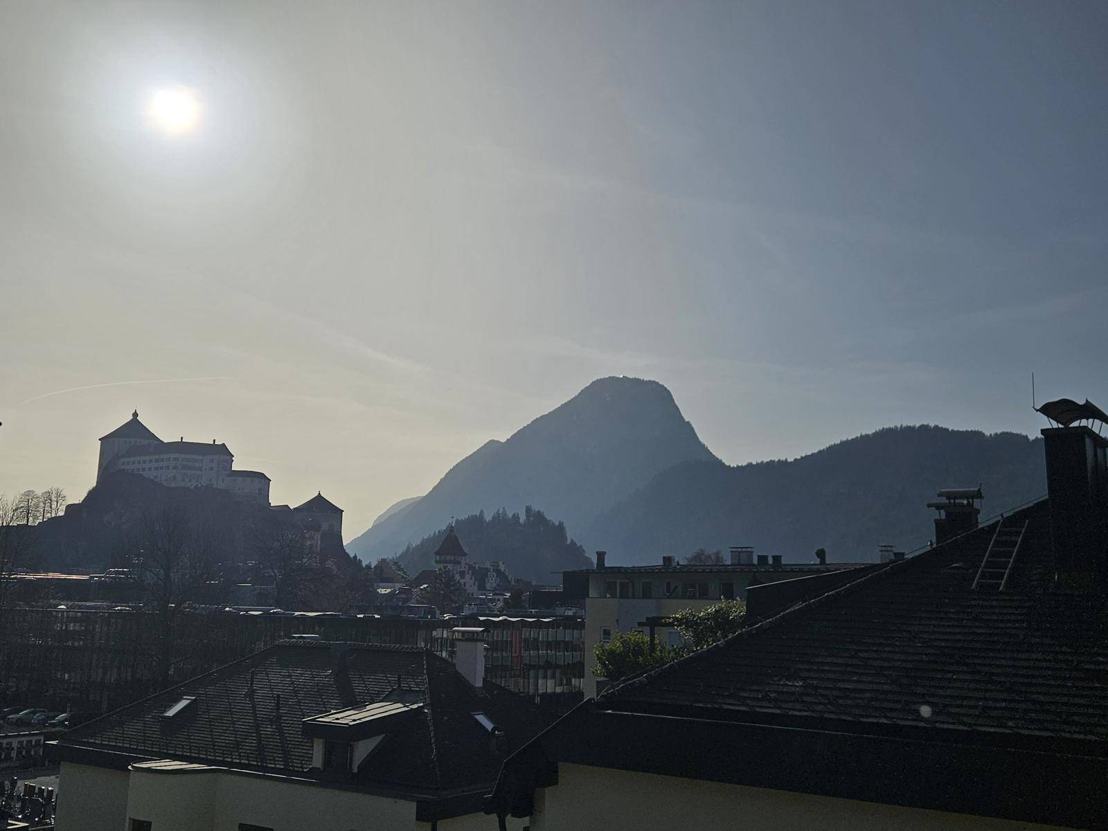 Panoramablick über die Dächer der Stadt mit einer historischen Burg und majestätischen Bergen im Hintergrund.
