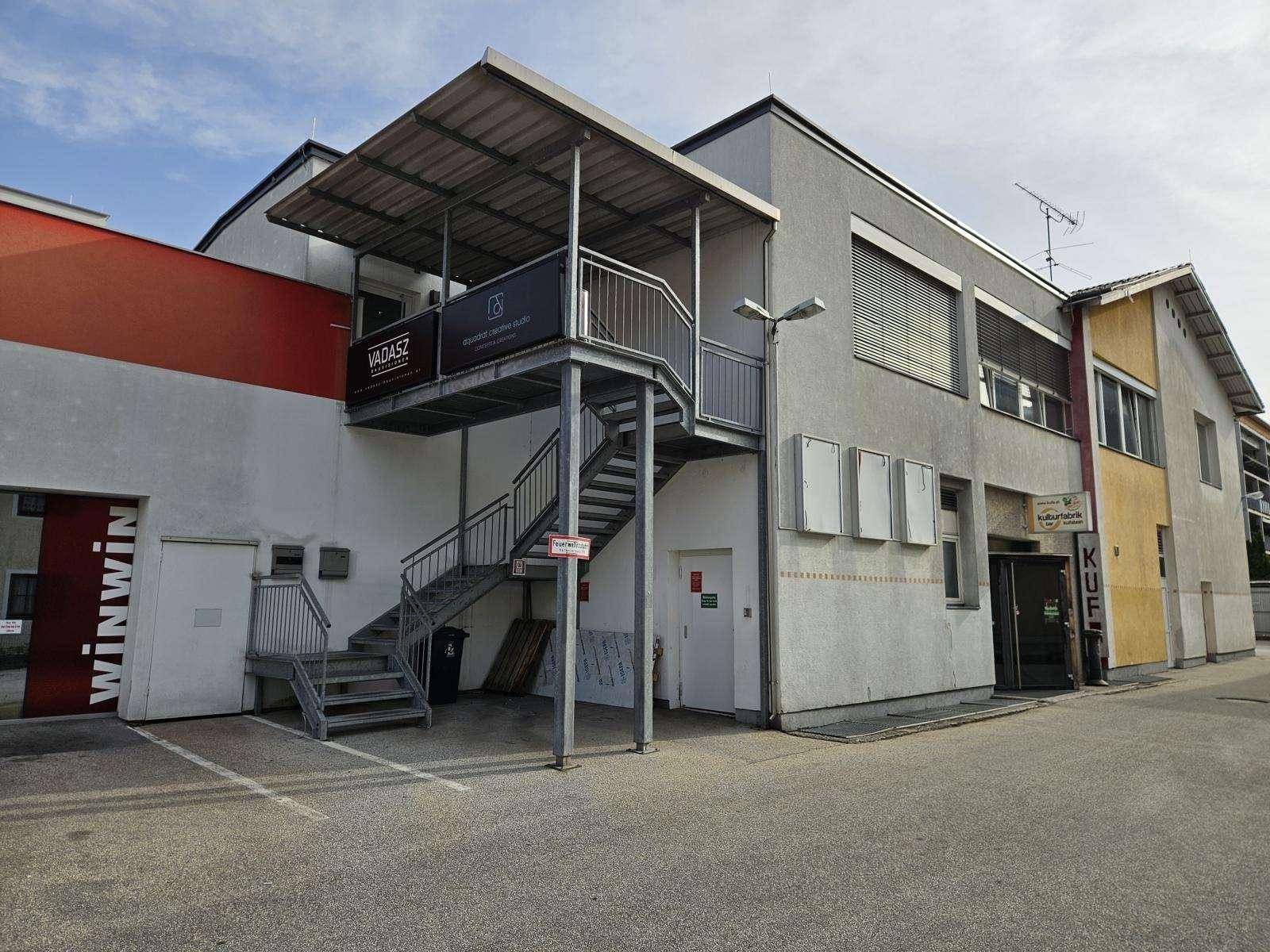 Rückansicht eines Geschäftsgebäudes mit Außentreppe, Parkplätzen und verschiedenen Fassaden.