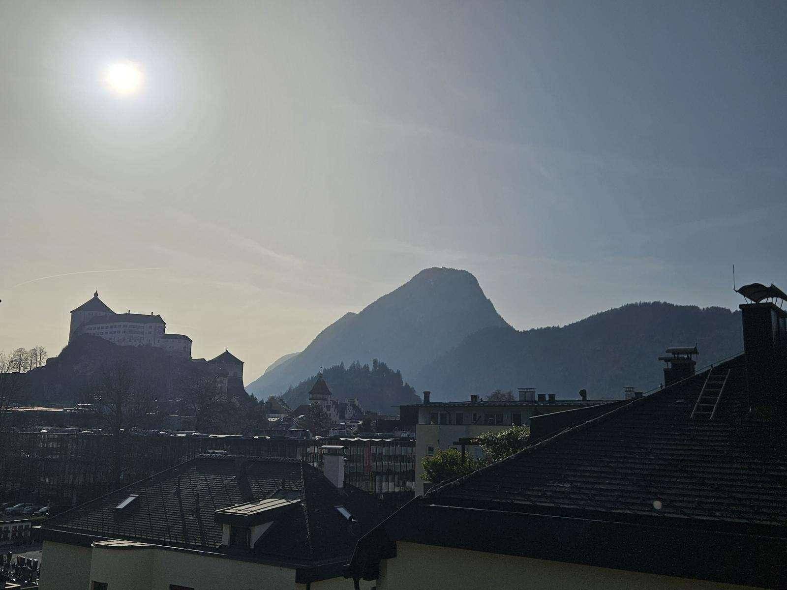 Weitblick auf eine historische Burg und majestätische Berge unter hellem Himmel.