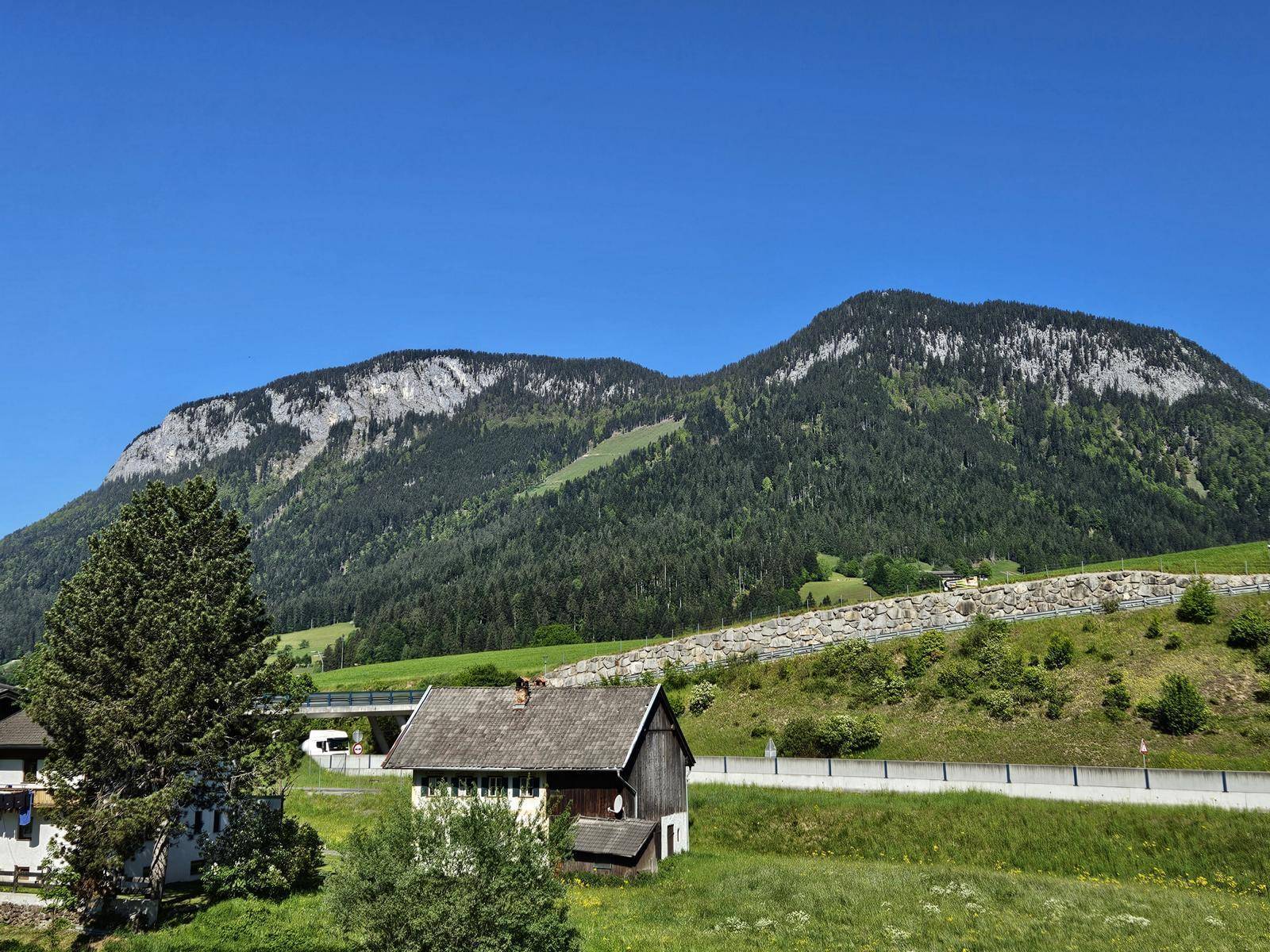 Panoramablick auf eine beeindruckende Bergkette mit bewaldeten Hängen und einer Straße im Vordergrund.