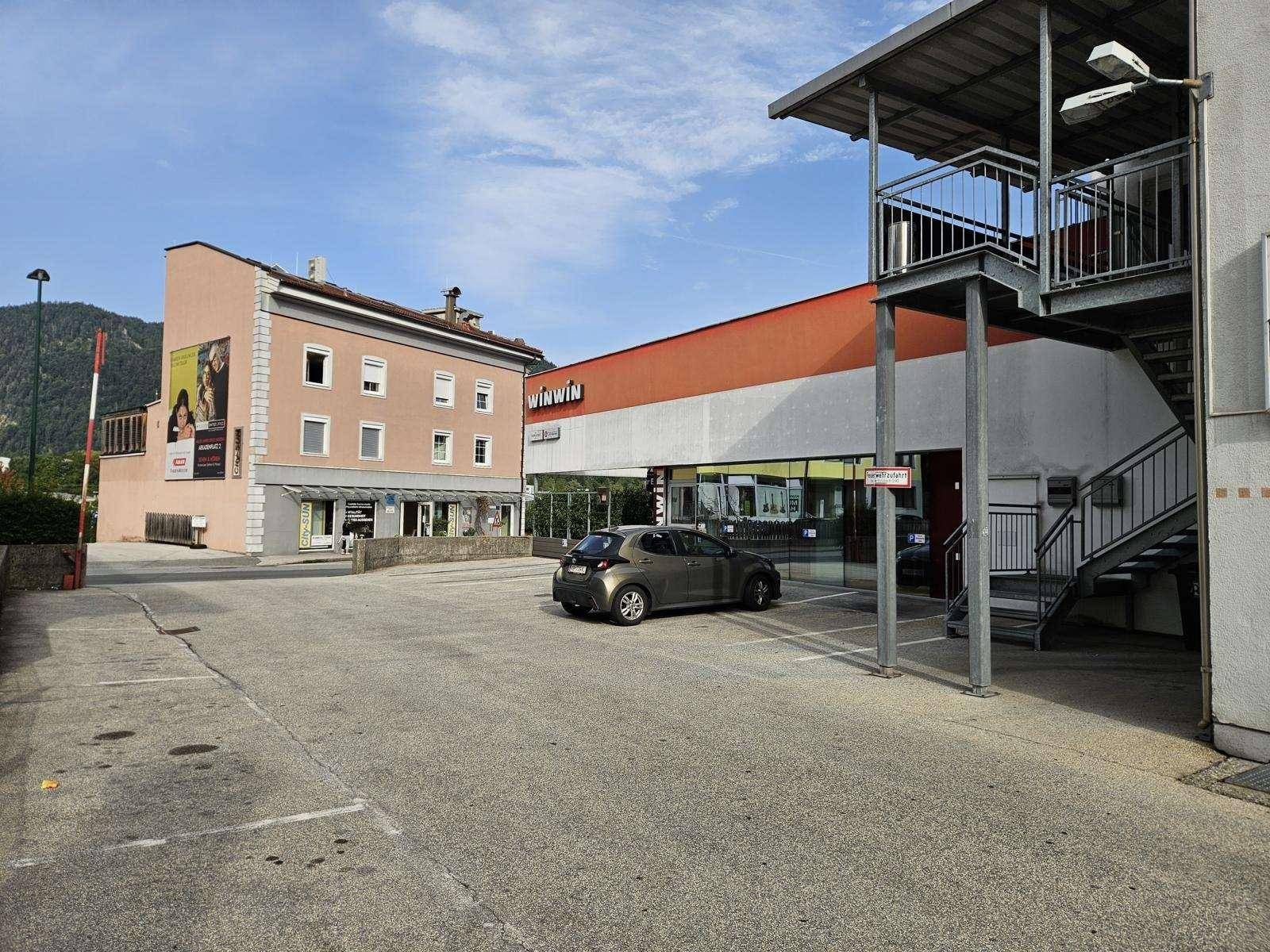 Ansicht eines Geschäftsgebäudes mit Parkplatz, Außentreppe und angrenzenden Gebäuden.