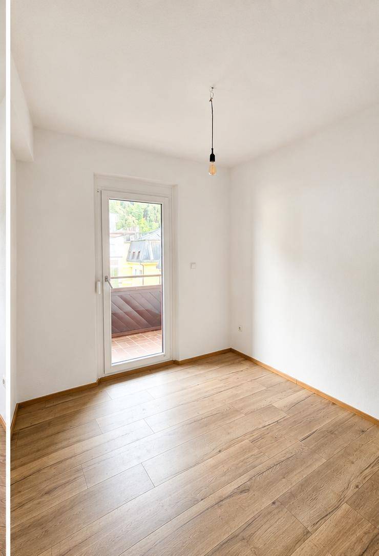 Leeres Schlafzimmer mit Balkonzugang und Holzboden, bietet viel Tageslicht und Gestaltungsmöglichkeiten.