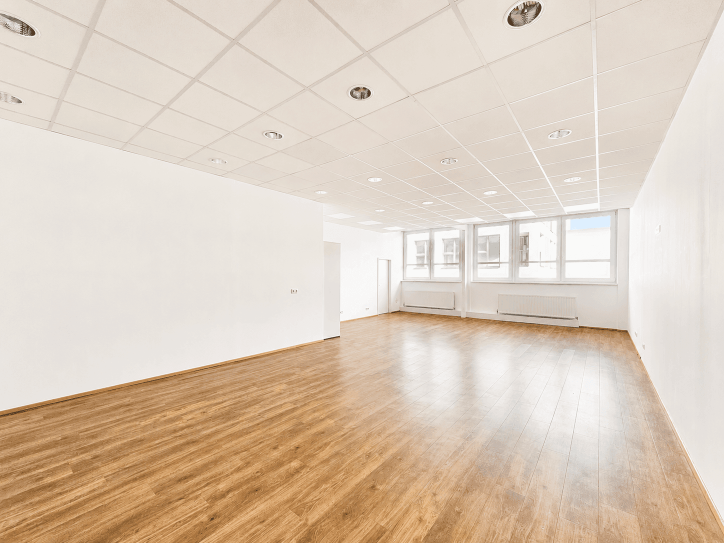 Großer, heller Gewerberaum mit vielen Fenstern, Laminatboden und abgehängter Decke.