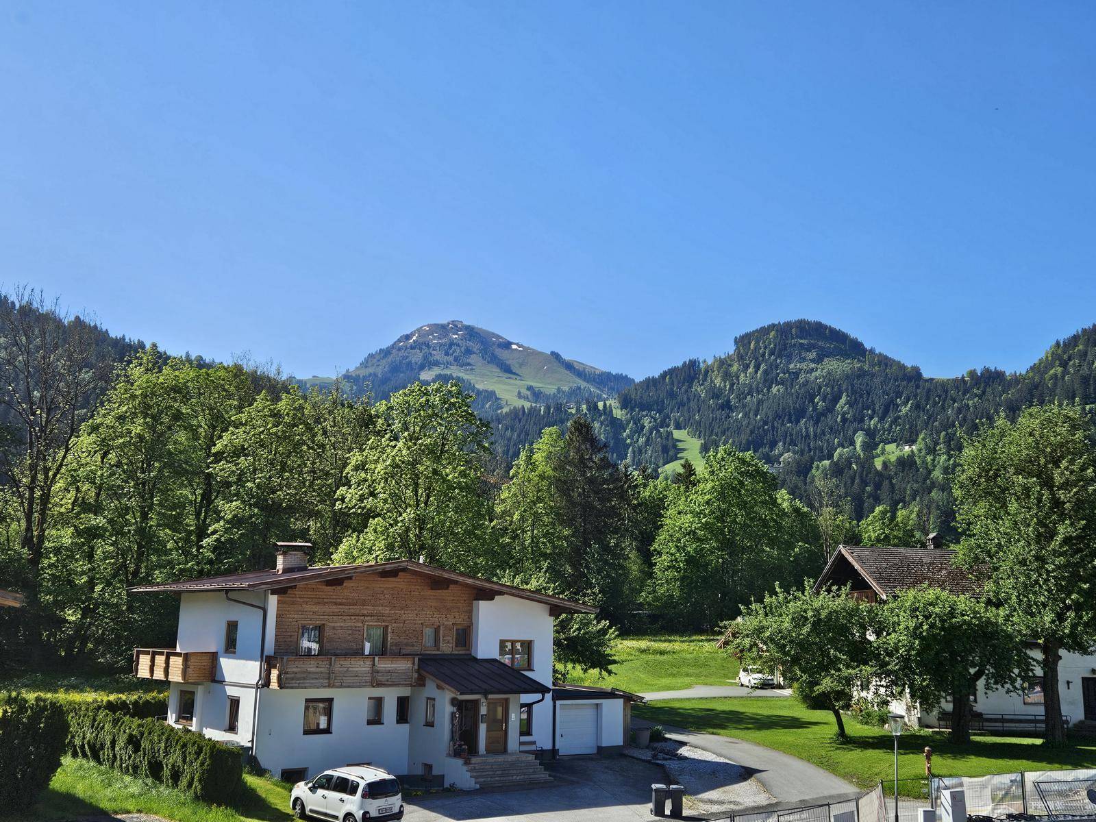Traditionelles Haus in ländlicher Umgebung mit Blick auf die bewaldeten Berge unter blauem Himmel.