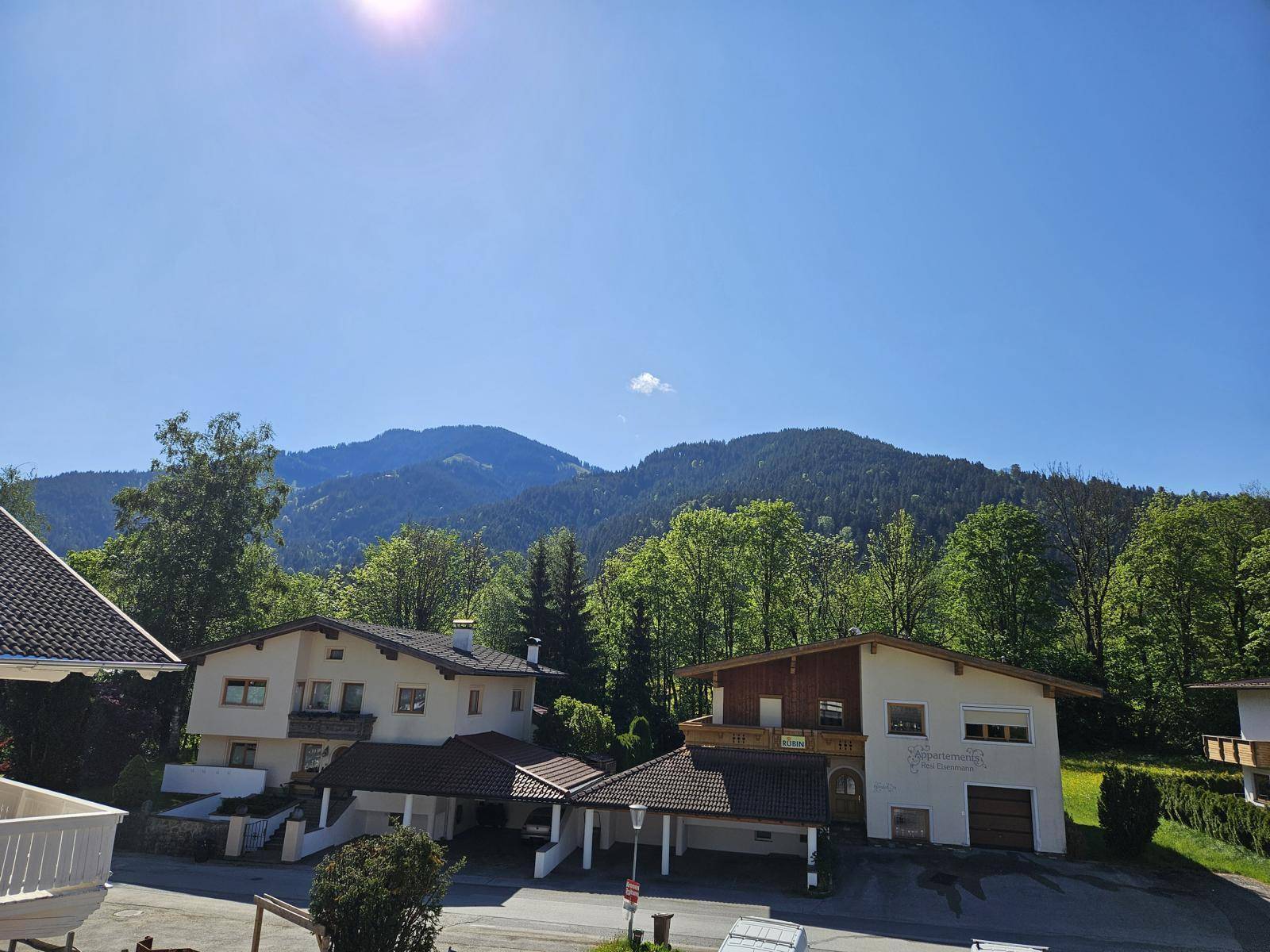Sonniger Blick auf traditionelle Häuser und die bewaldeten Berge in der Ferne.