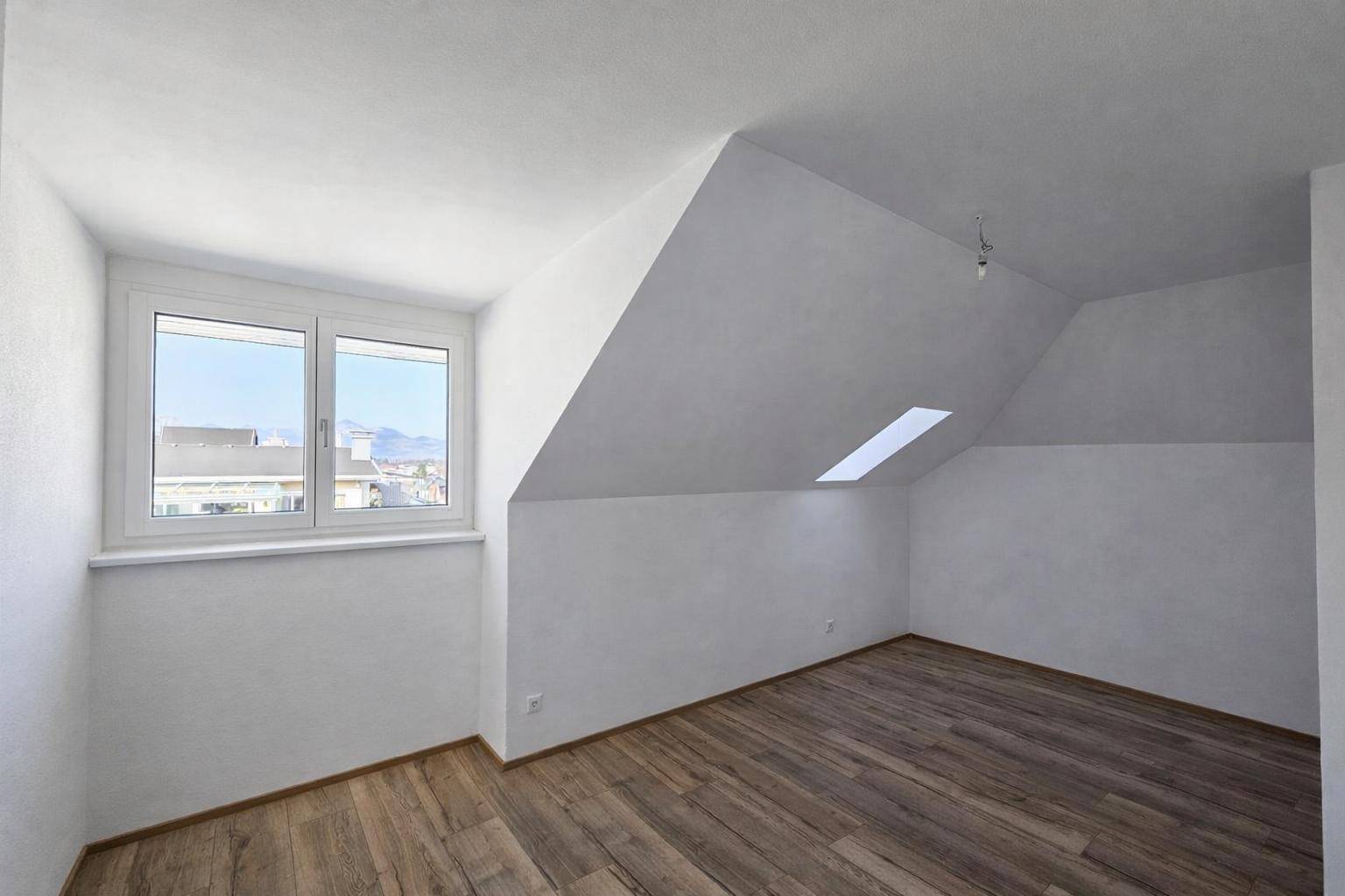Leeres Schlafzimmer im Dachgeschoss mit Holzboden, schrägen Wänden und einem Fenster, bereit zur Einrichtung.