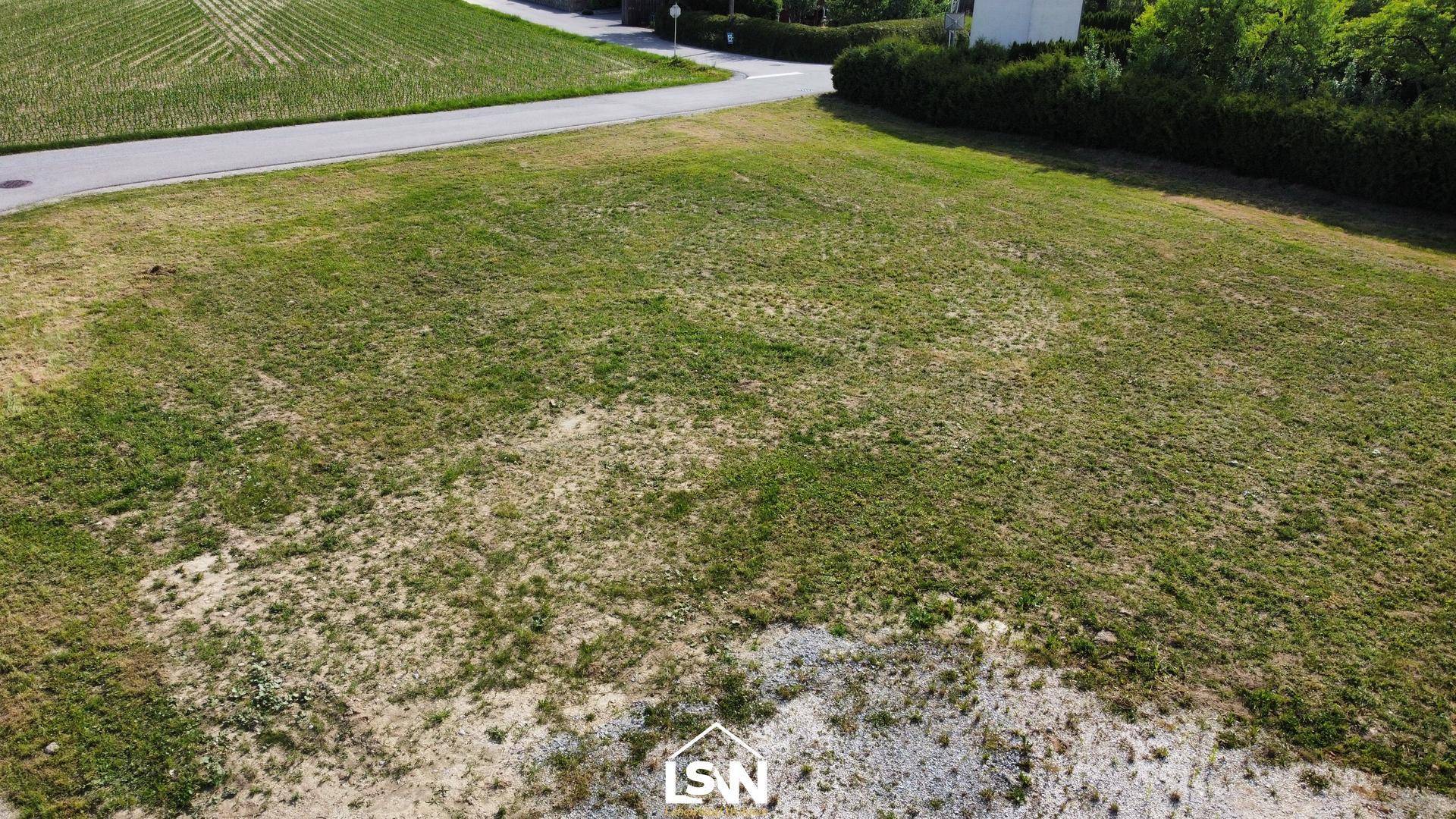 Nahaufnahme des unbebauten Grundstücks mit Grasfläche und angrenzender Straße in ländlicher Lage.