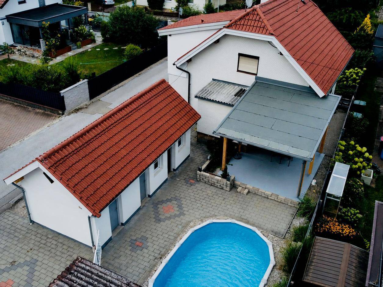 Detaillierte Luftaufnahme des Hauses mit gepflastertem Hof, Nebengebäude und einem ovalen Swimmingpool.