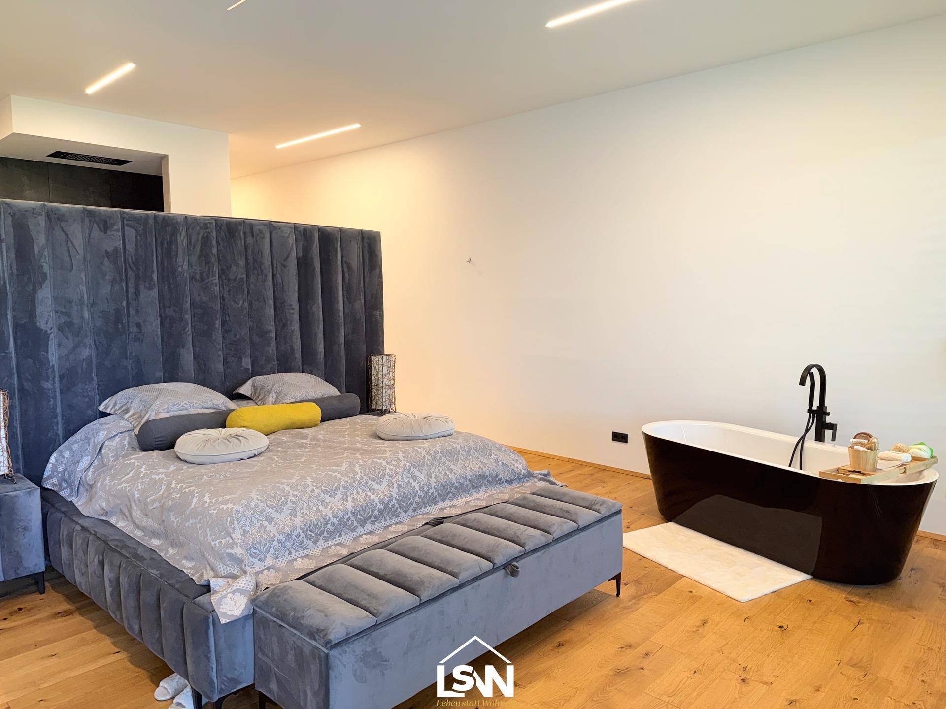 Modernes Schlafzimmer mit großem Bett, Holzboden und freistehender Badewanne.