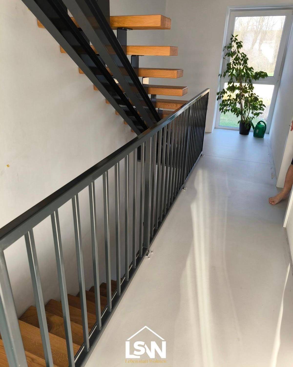Heller Flur mit moderner Treppe aus Holz und Metall sowie einem Fenster mit Blick ins Grüne.