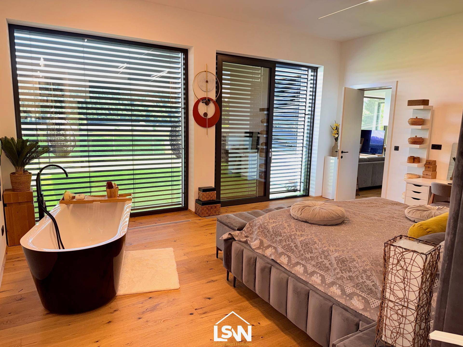 Helles Schlafzimmer mit großem Bett, Holzboden und freistehender Badewanne vor dem Fenster.