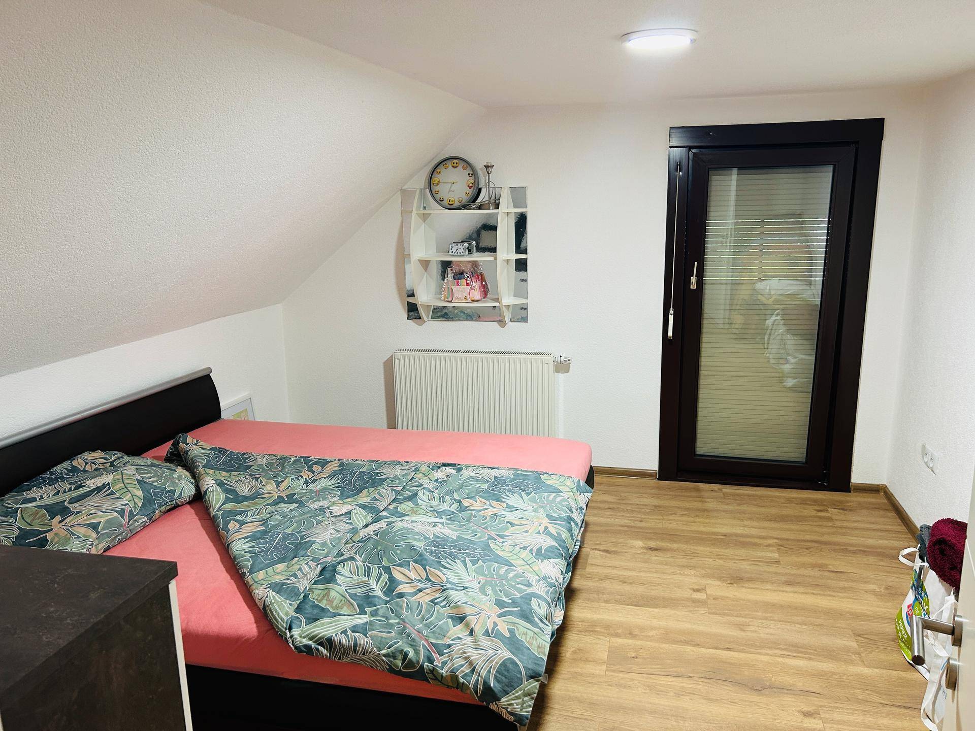 Gemütliches Schlafzimmer im Dachgeschoss mit schräger Decke, Laminatboden und einem Fenster.