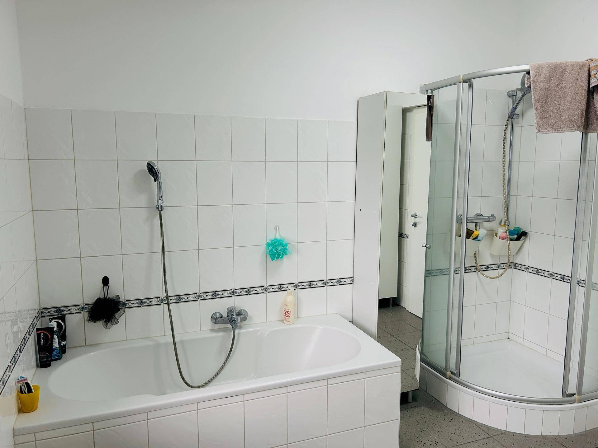 Helles Badezimmer mit Badewanne, Duschkabine und weißen Fliesen, funktional eingerichtet.