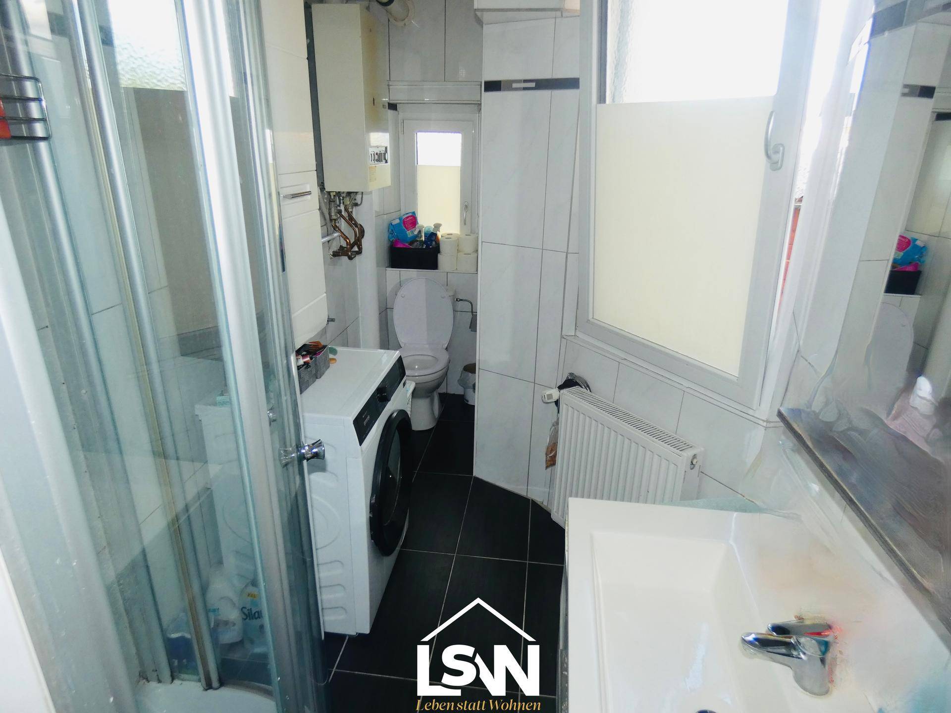 Kompaktes Badezimmer mit Dusche, WC, Waschbecken und Waschmaschine.