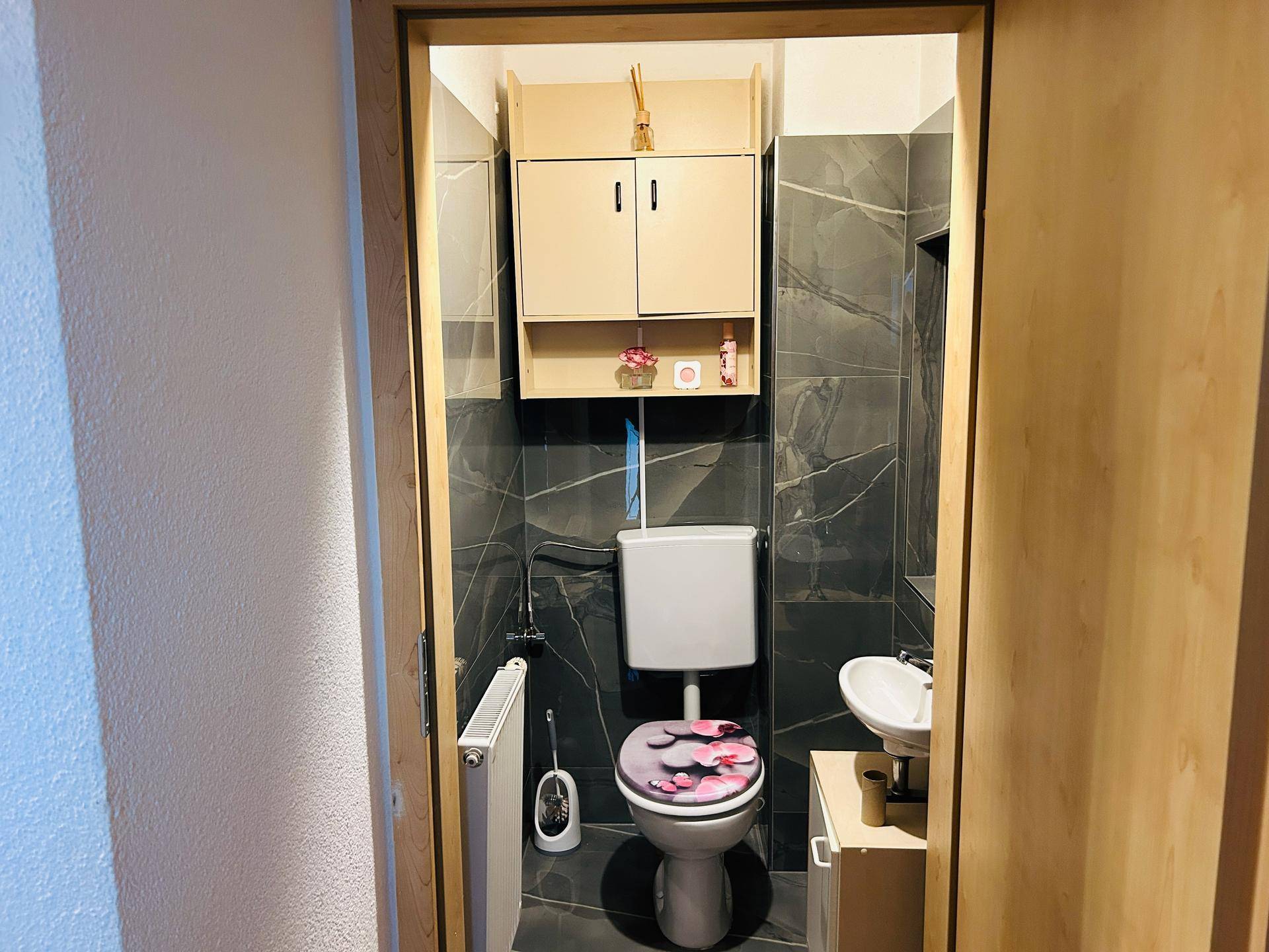 Kleines Gäste-WC mit modernen dunklen Fliesen, Toilette und einem kompakten Waschbecken.