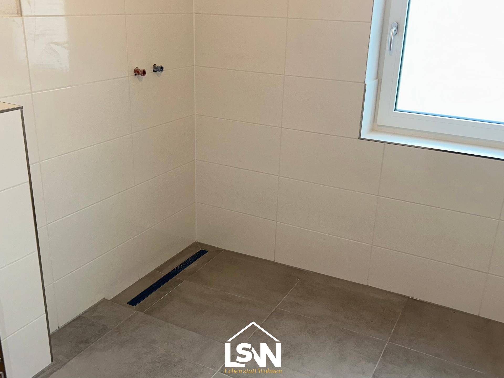 Modern geflieste Duschkabine mit Bodeneinlauf und Fenster für natürliche Belüftung.