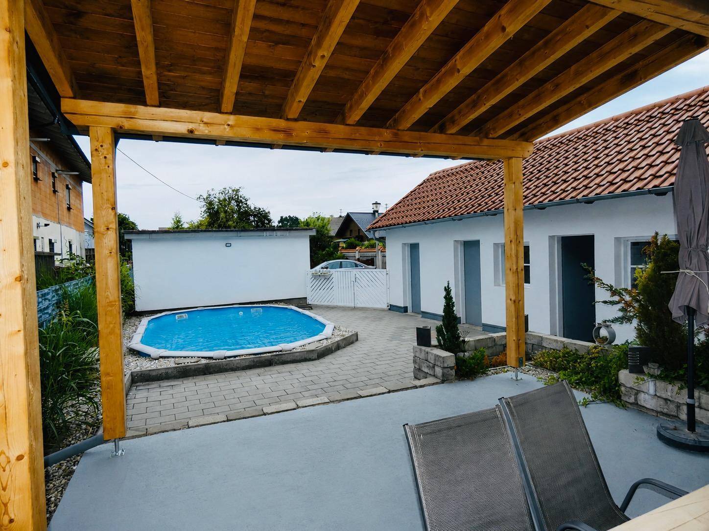 Überdachte Terrasse mit Holzkonstruktion und Liegestühlen, direkt neben dem Swimmingpool gelegen.