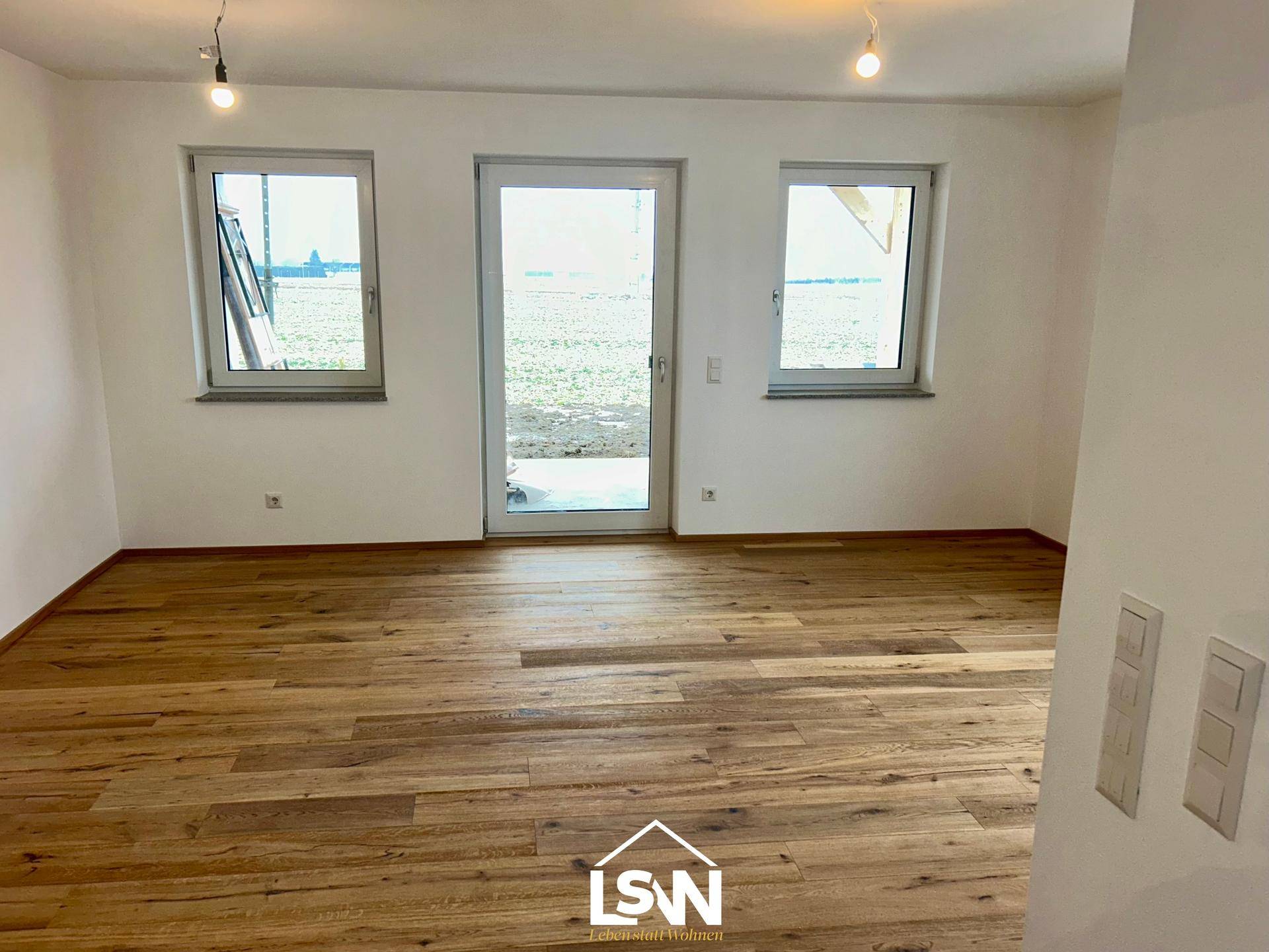 Lichtdurchfluteter Raum mit Holzboden, großer Glastür und Fenstern, die Zugang zum Außenbereich bieten.