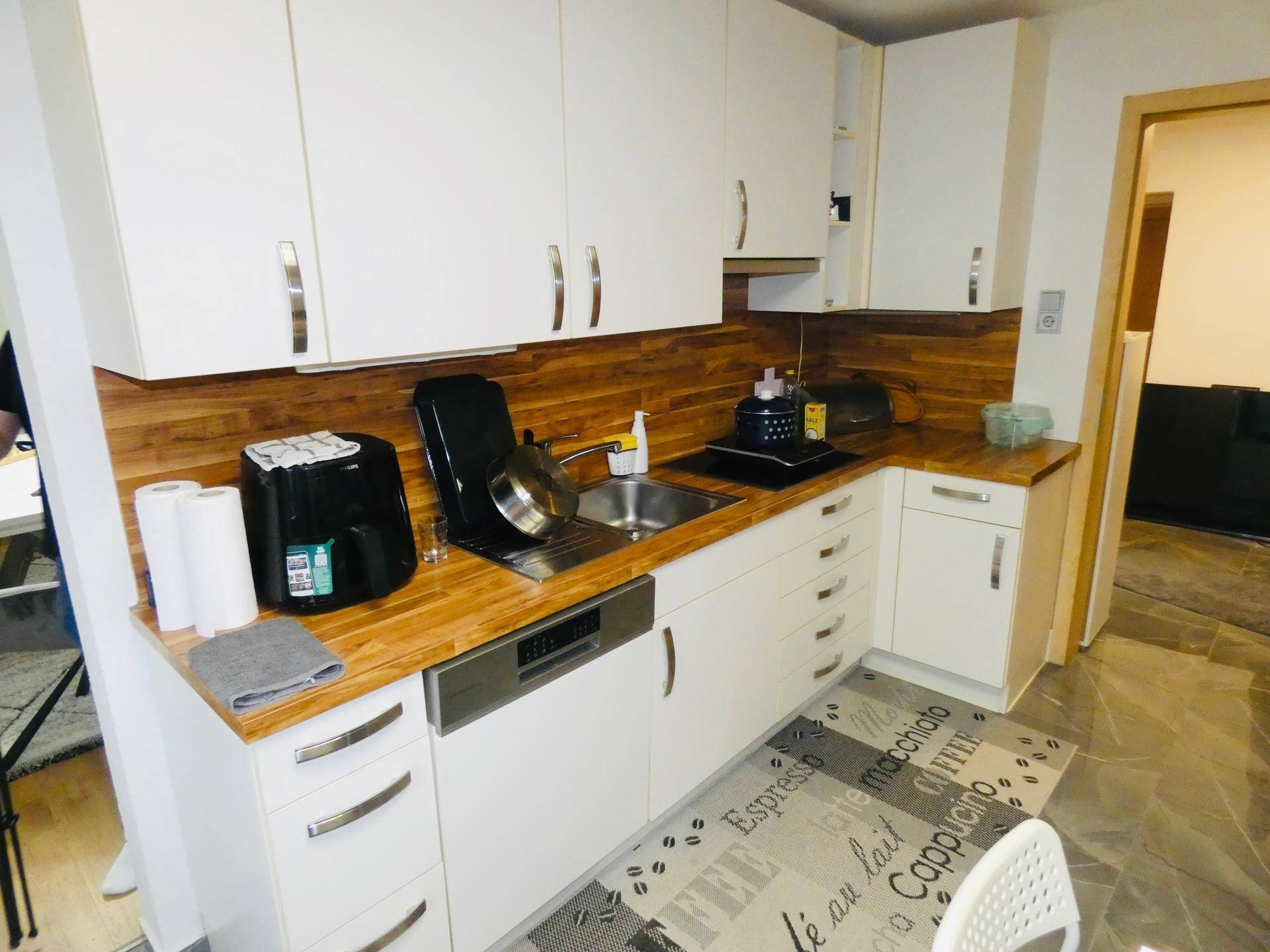 Funktionale Küche mit weißen Schränken, Holz-Arbeitsplatten und integriertem Geschirrspüler.