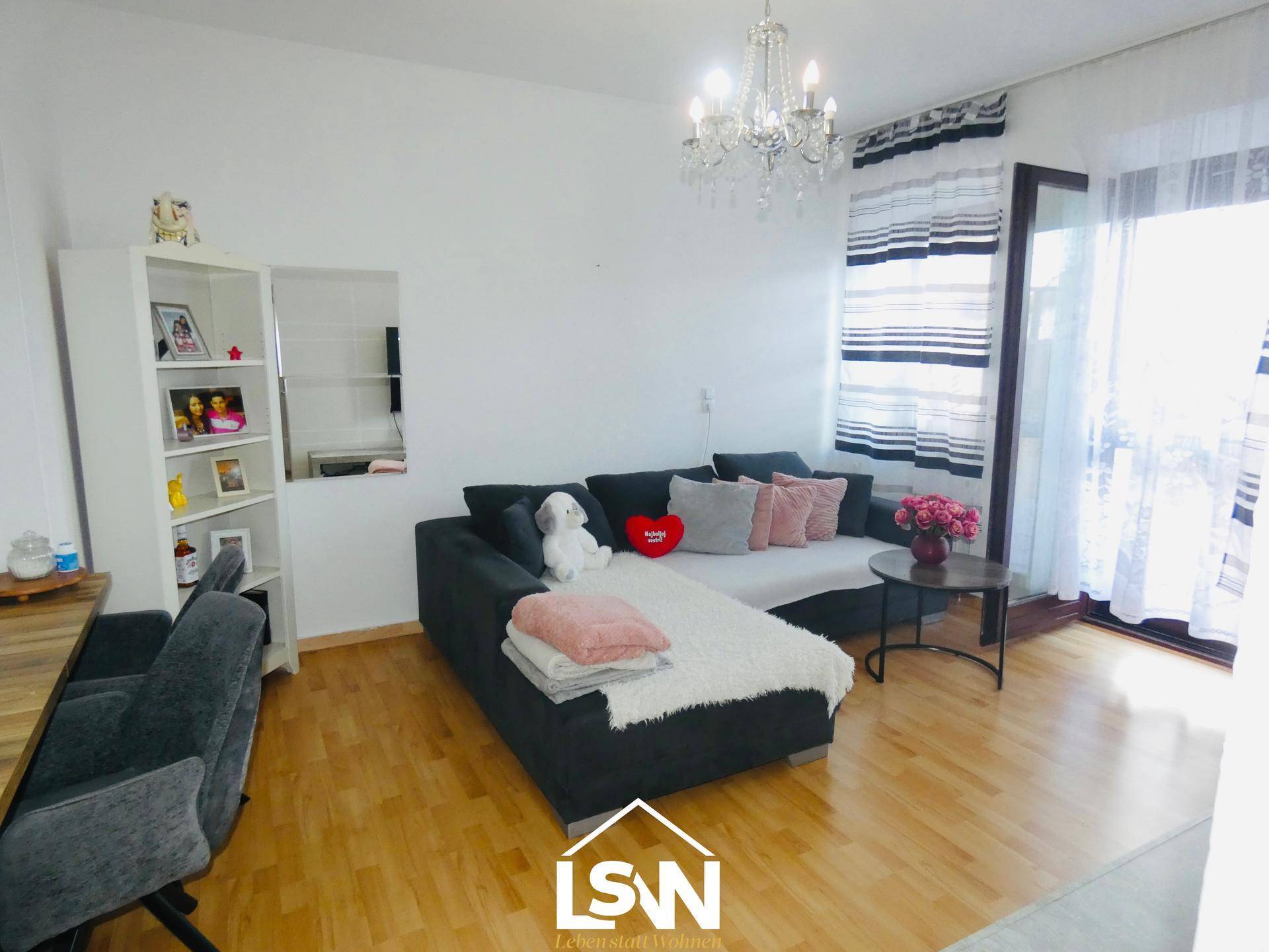 Helles Wohnzimmer mit großem Ecksofa, Kronleuchter und Zugang zu einem Balkon.