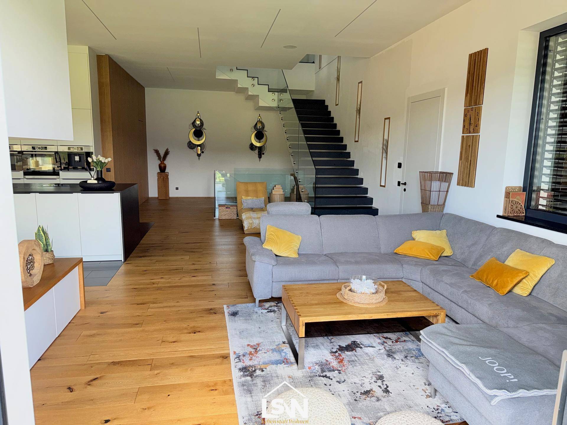 Geräumiges Wohnzimmer mit bequemer Couch, Holzboden und offener Treppe.