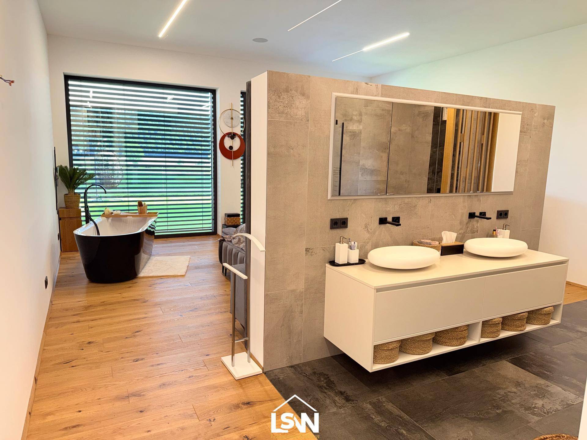 Großzügiges Badezimmer mit Doppelwaschbecken und Blick auf die freistehende Badewanne im Schlafzimmer.