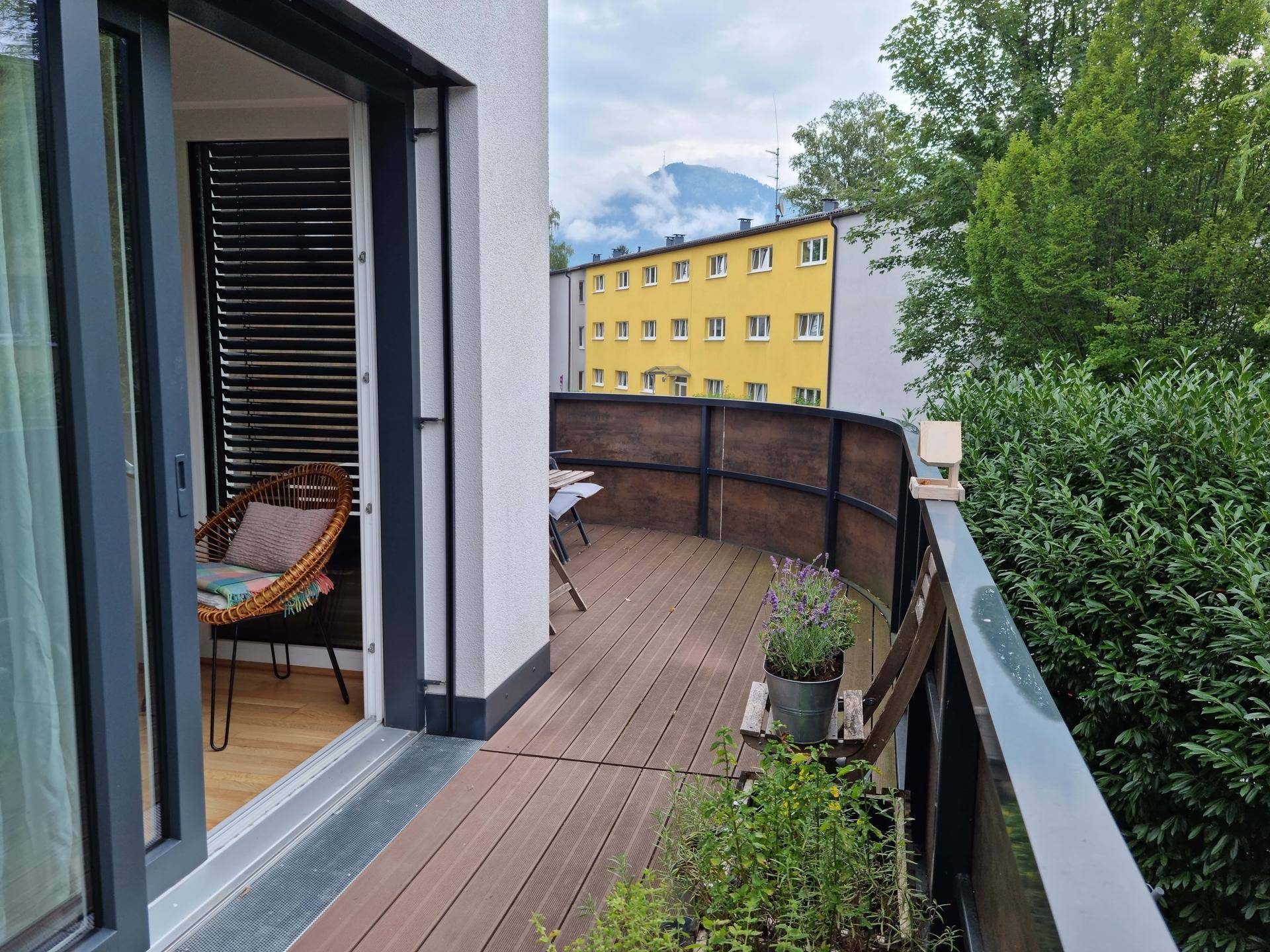 Geräumiger Balkon mit Holzboden, Sitzgelegenheiten und Blick auf die Berge.