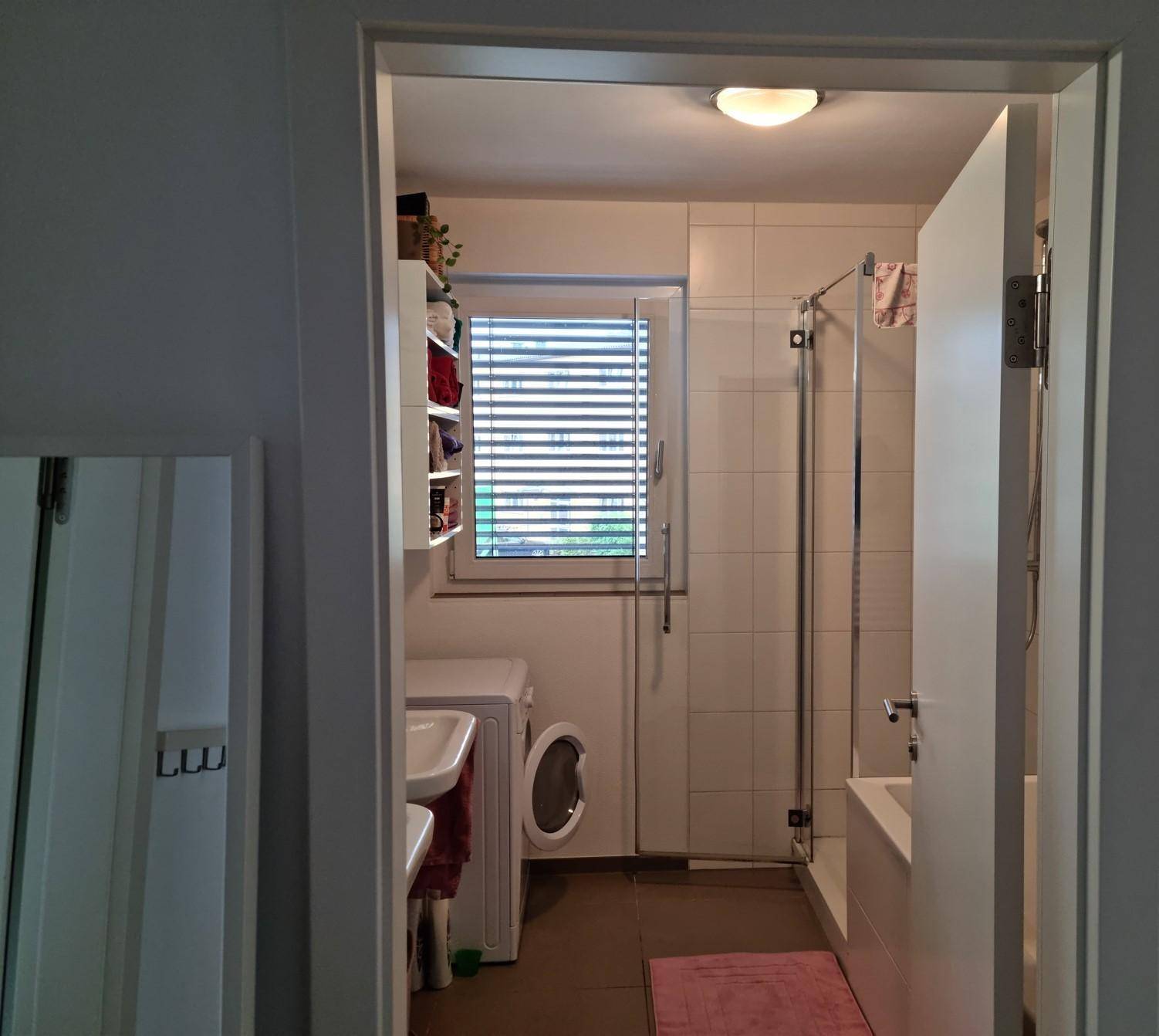 Badezimmer mit Badewanne, Dusche, Waschmaschine und Fenster für Tageslicht.
