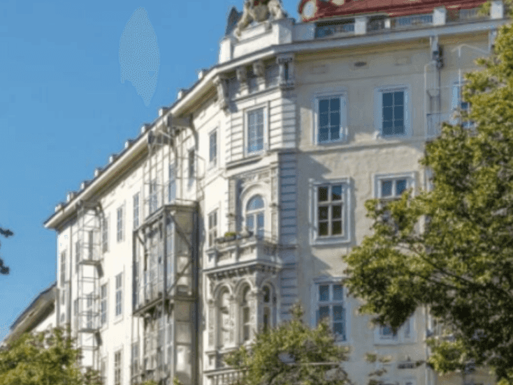 Historisches Gebäude mit klassischer Architektur, vielen Fenstern und Bäumen im Vordergrund.