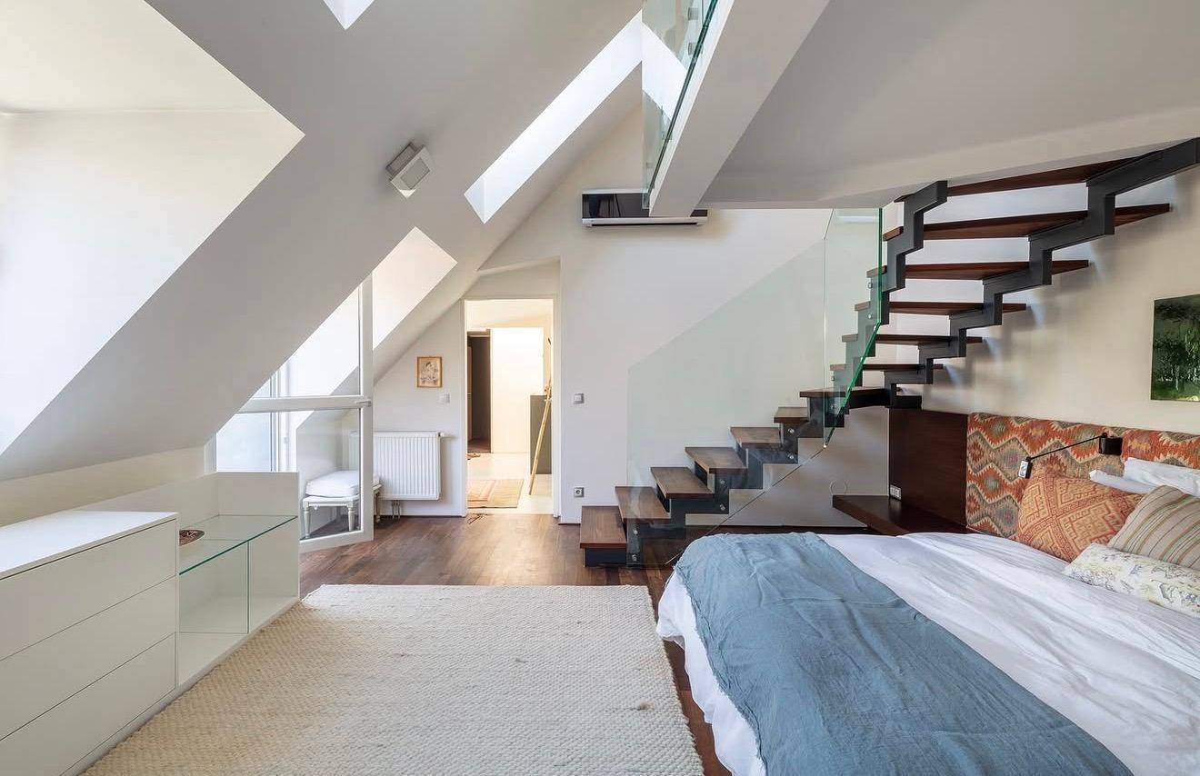 Modernes Schlafzimmer mit Holzboden, Dachschrägen und offener Treppe zu einer oberen Ebene.