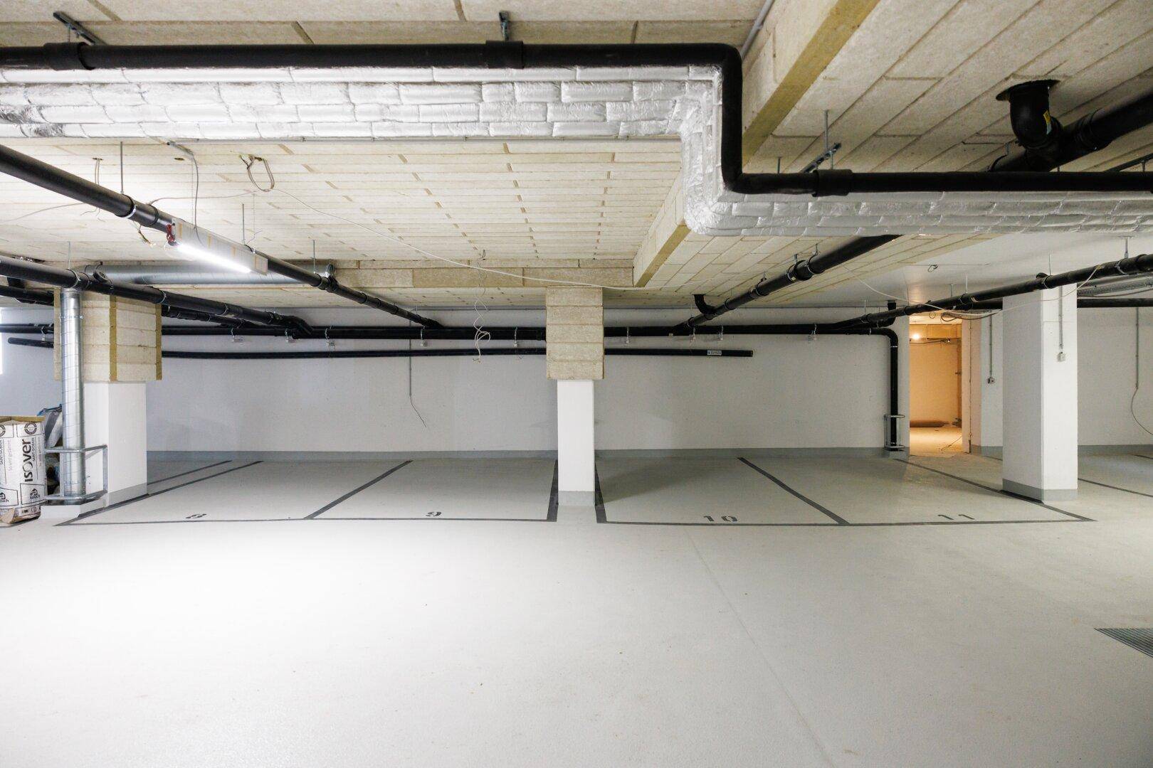 Geräumige Tiefgarage mit markierten Stellplätzen und sichtbaren Installationen an der Decke.