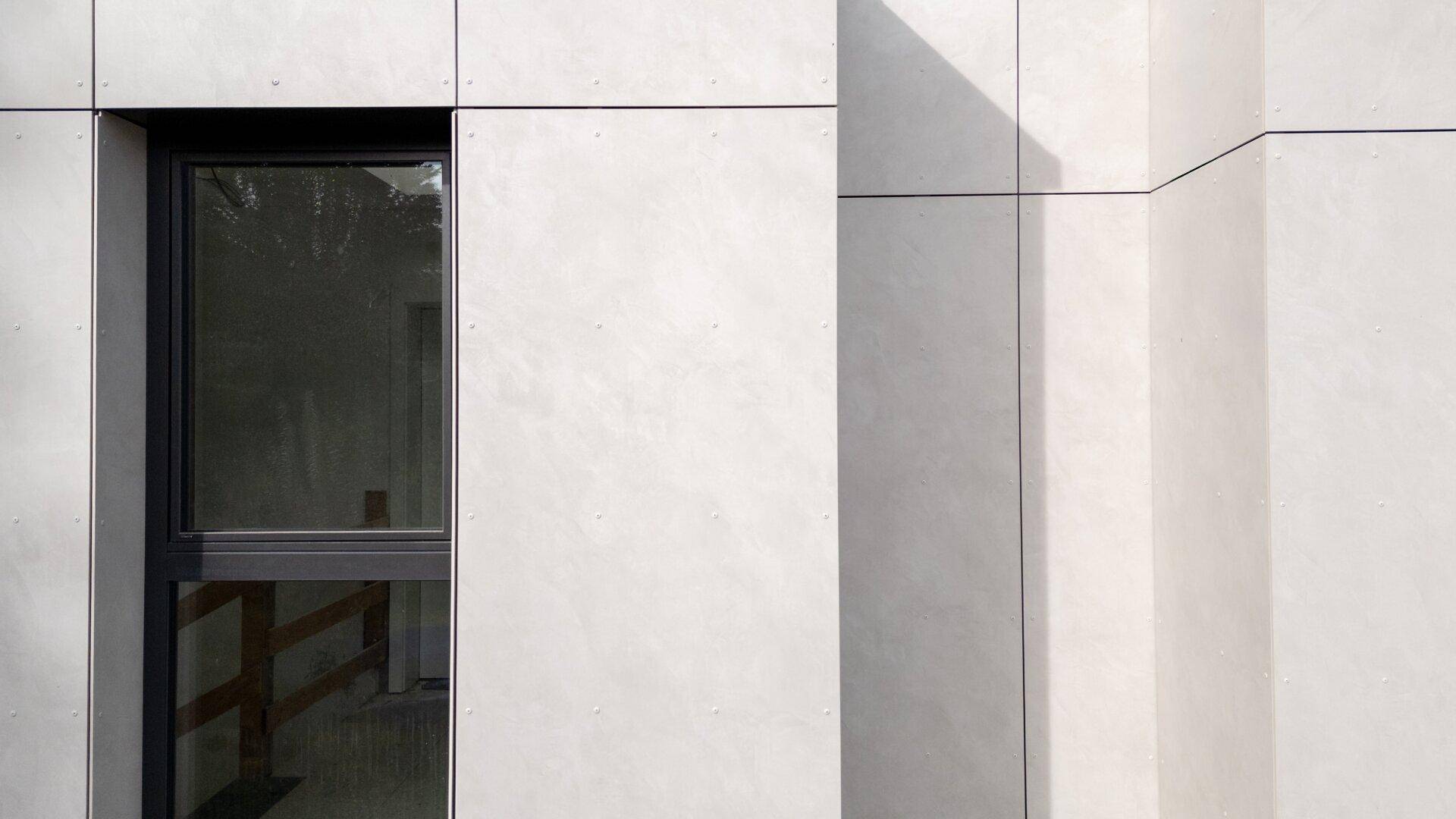Detailansicht einer modernen Gebäudefassade mit grauen Paneelen und einem Fenster.