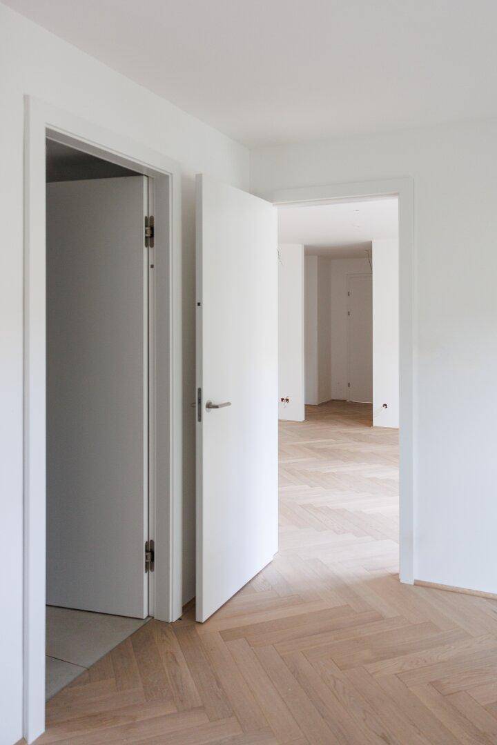 Heller Flur mit Fischgrätparkett und offenen weißen Türen, der zu weiteren Räumen führt.