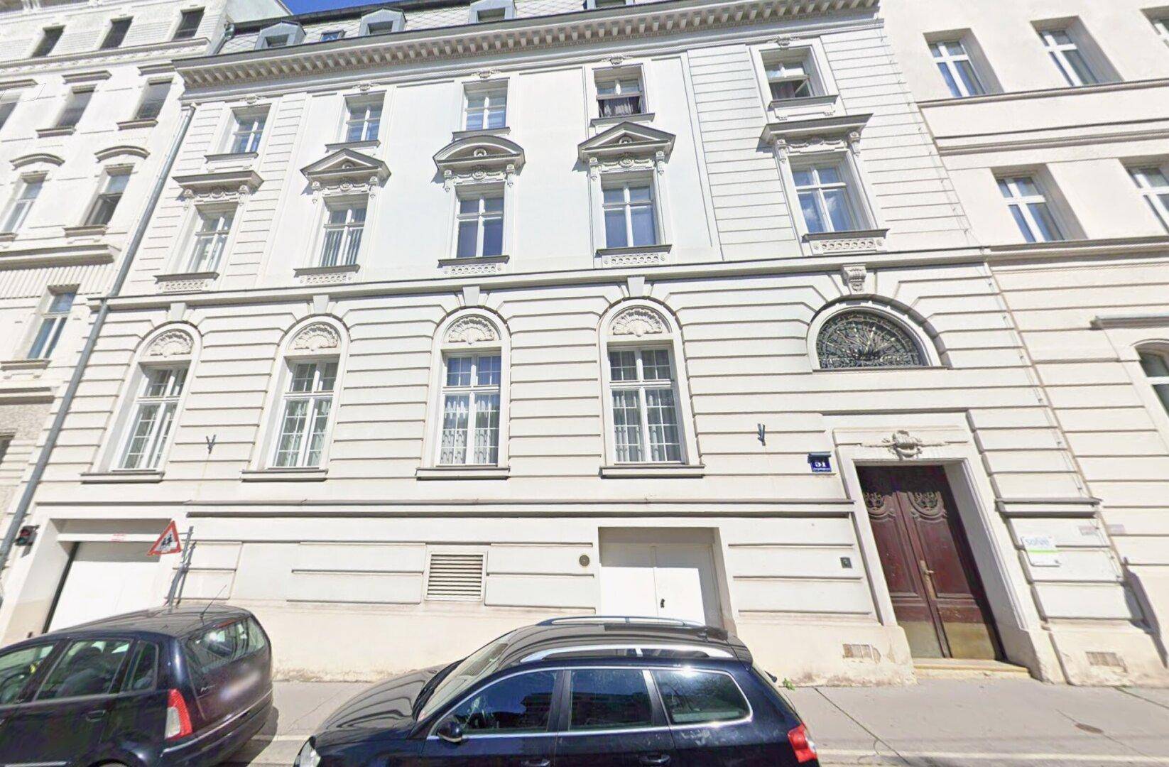 Klassische Fassade eines Altbaus mit eleganten Fenstern und einem markanten Holztor.