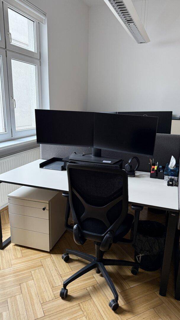 Moderner Arbeitsplatz in einem Büro mit zwei Monitoren, ergonomischem Stuhl und viel Tageslicht.