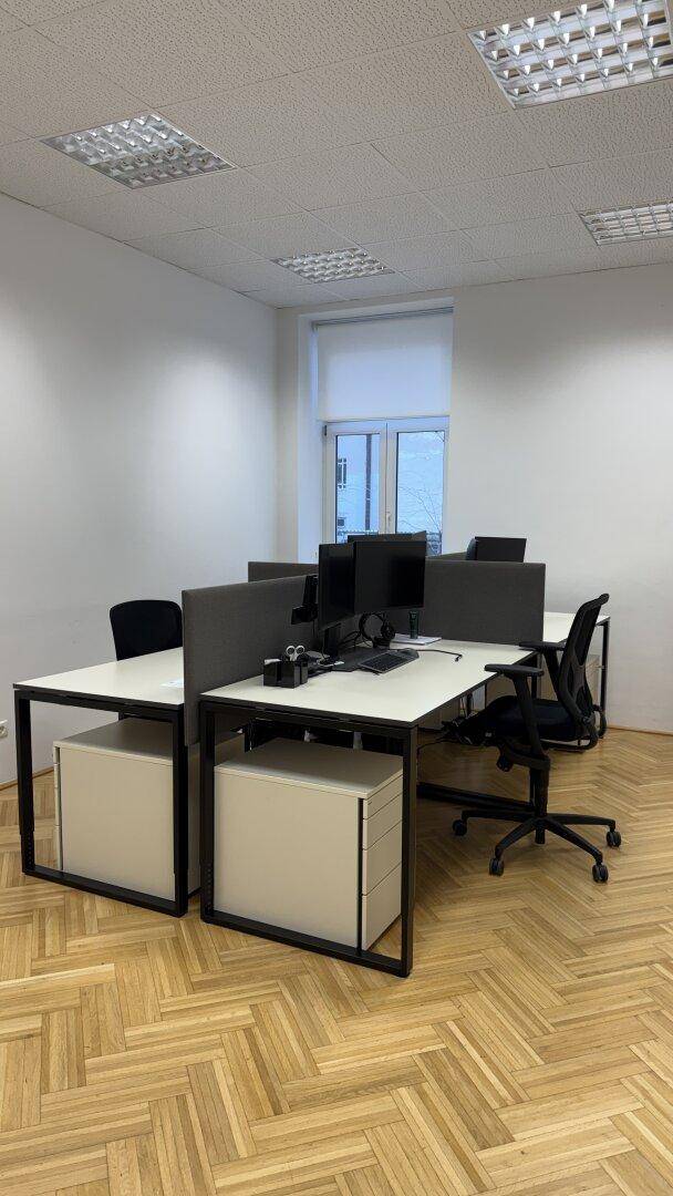 Helles Großraumbüro mit mehreren Arbeitsplätzen, ergonomischen Stühlen und großen Fenstern.