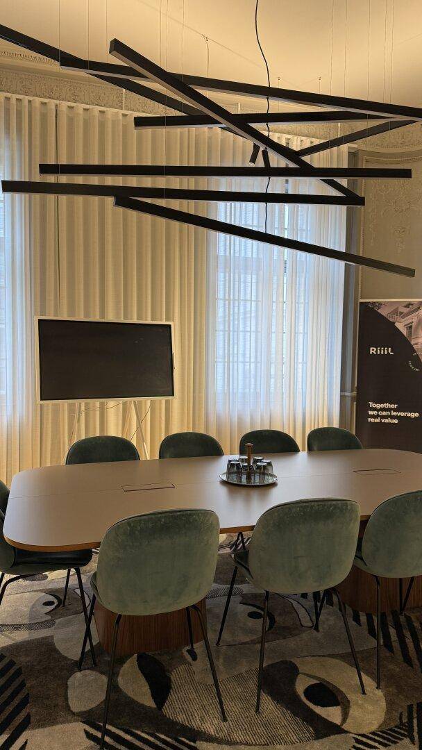 Moderner Konferenzraum mit großem Tisch, bequemen Stühlen und einem an der Wand montierten Bildschirm.