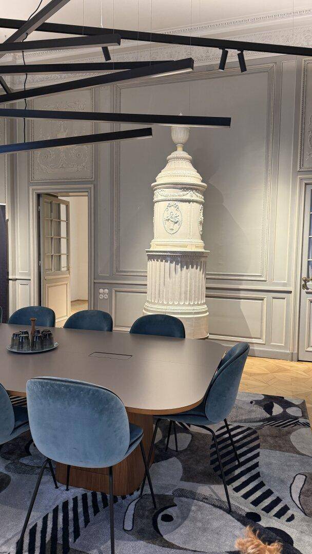 Eleganter Konferenzraum mit traditionellem Kachelofen, Holzboden und modernen Stühlen um einen großen Tisch.