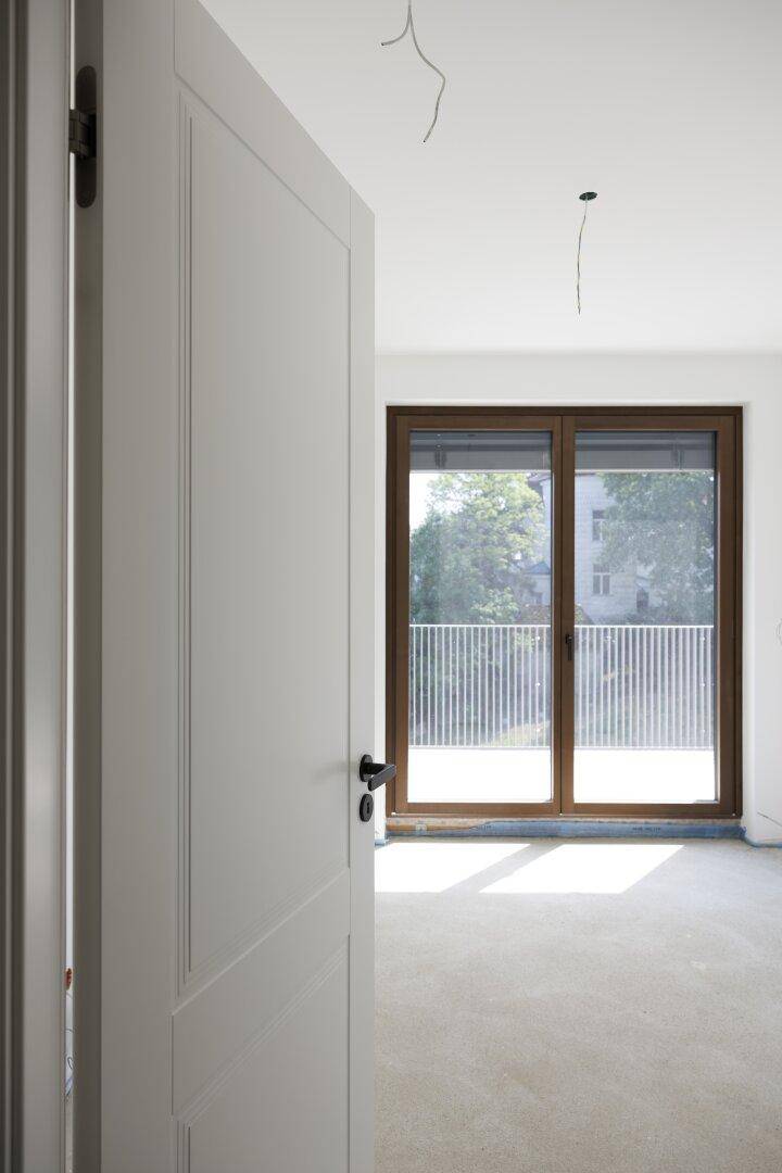 Heller, unmöblierter Raum mit weißer Tür und großem Fenster, das auf einen Balkon führt.
