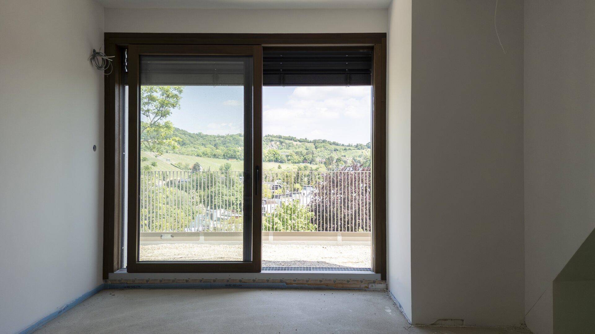 Leerer Raum mit großer Glasschiebetür, die einen weiten Blick ins Grüne und viel Licht bietet.