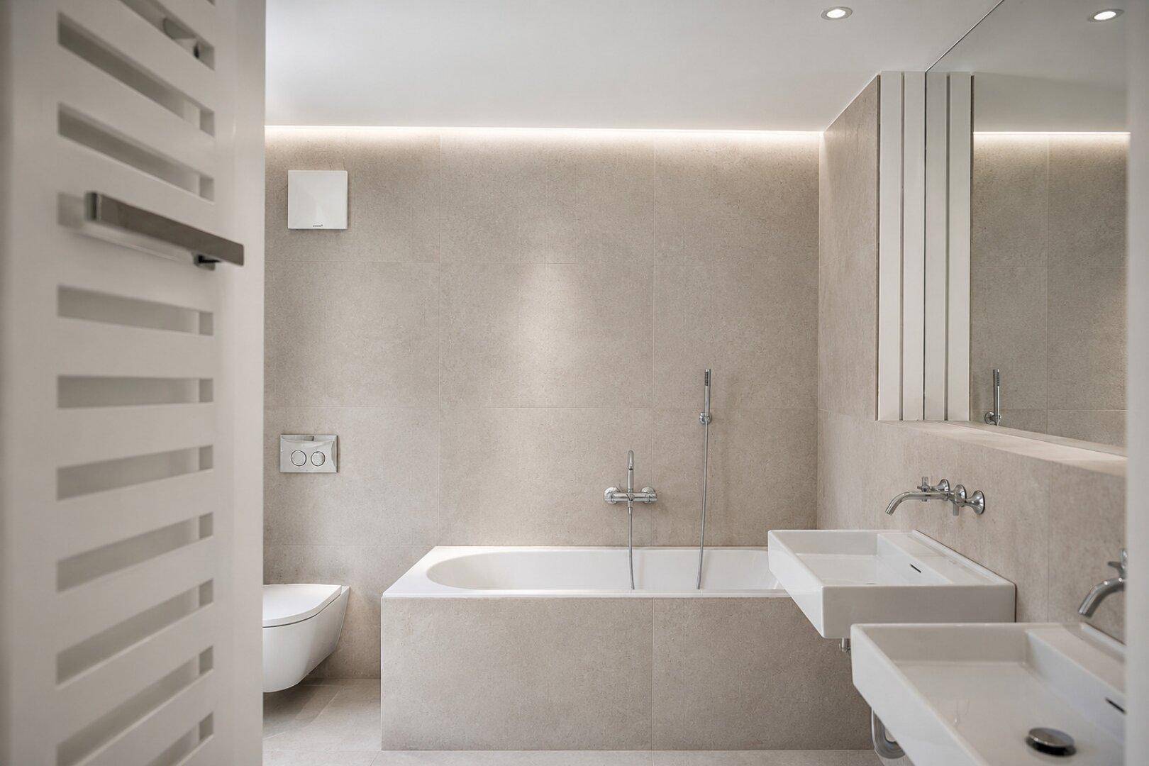 Modernes Badezimmer mit Doppelwaschbecken, Badewanne und eleganten beigefarbenen Fliesen.