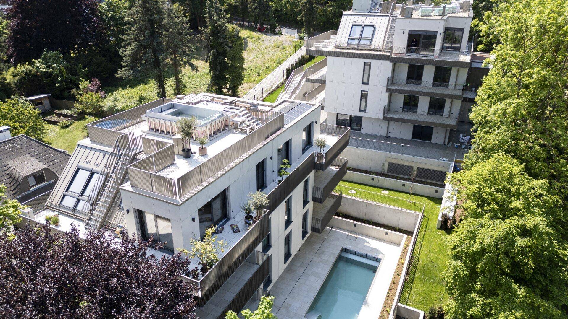 Luftaufnahme von zwei modernen Apartmentgebäuden mit Balkonen, Dachterrassen und einem Pool.