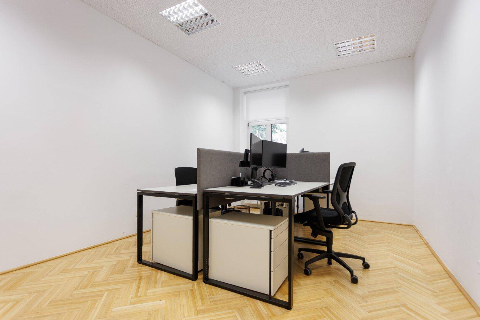 Modernes Büro mit vier Arbeitsplätzen, Fischgrätparkett und heller Deckenbeleuchtung.