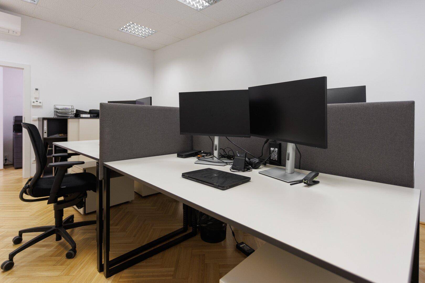 Detailansicht eines modernen Arbeitsplatzes mit zwei Monitoren und ergonomischem Bürostuhl.