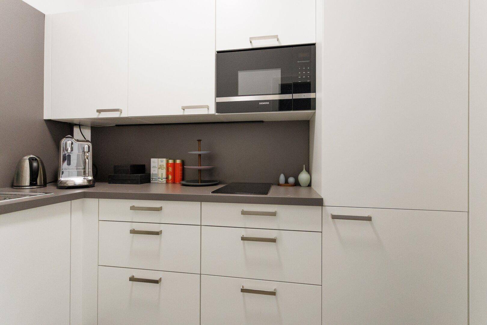 Moderne Küchenzeile mit weißen Schränken, integrierter Mikrowelle und Kaffeemaschine.