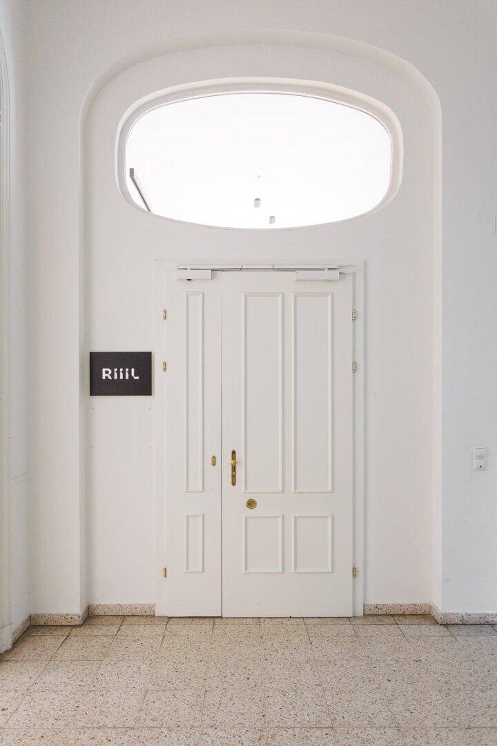Große weiße Doppeltür mit ovalem Oberlicht und einem Firmenlogo an der Wand.