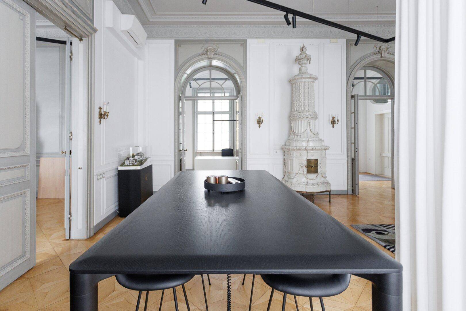 Essbereich mit langem schwarzem Tisch, passenden Hockern und elegantem Fischgrätparkett.