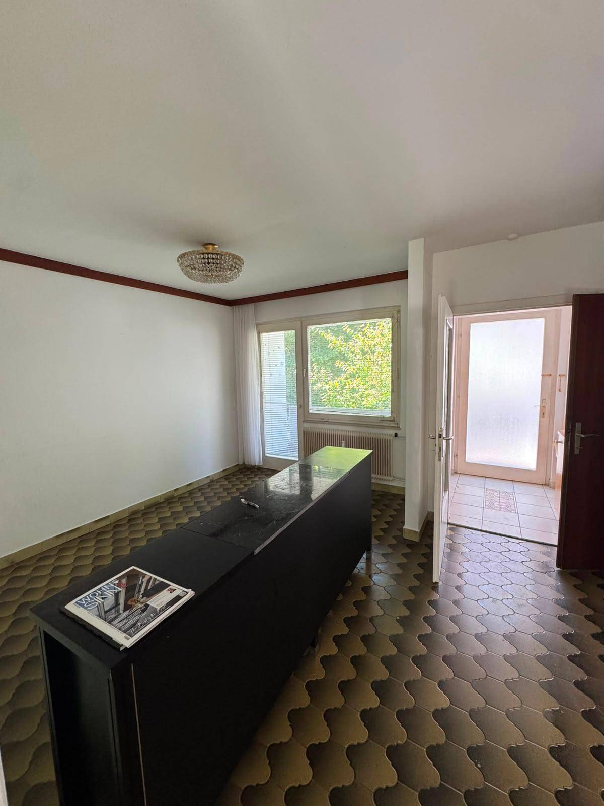 Heller Raum mit großem Fenster, gemustertem Fliesenboden und einer dunklen Theke.