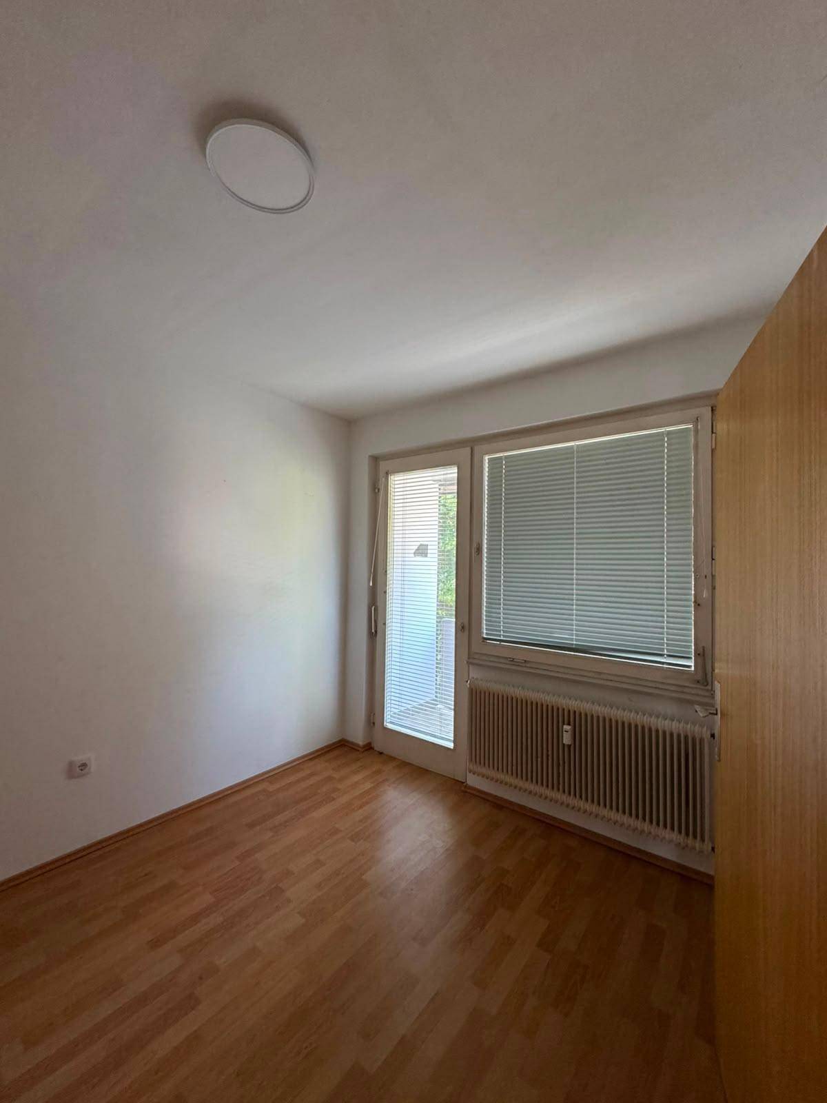 Schlafzimmer mit Laminatboden, großem Fenster und Zugang zu einem Balkon.