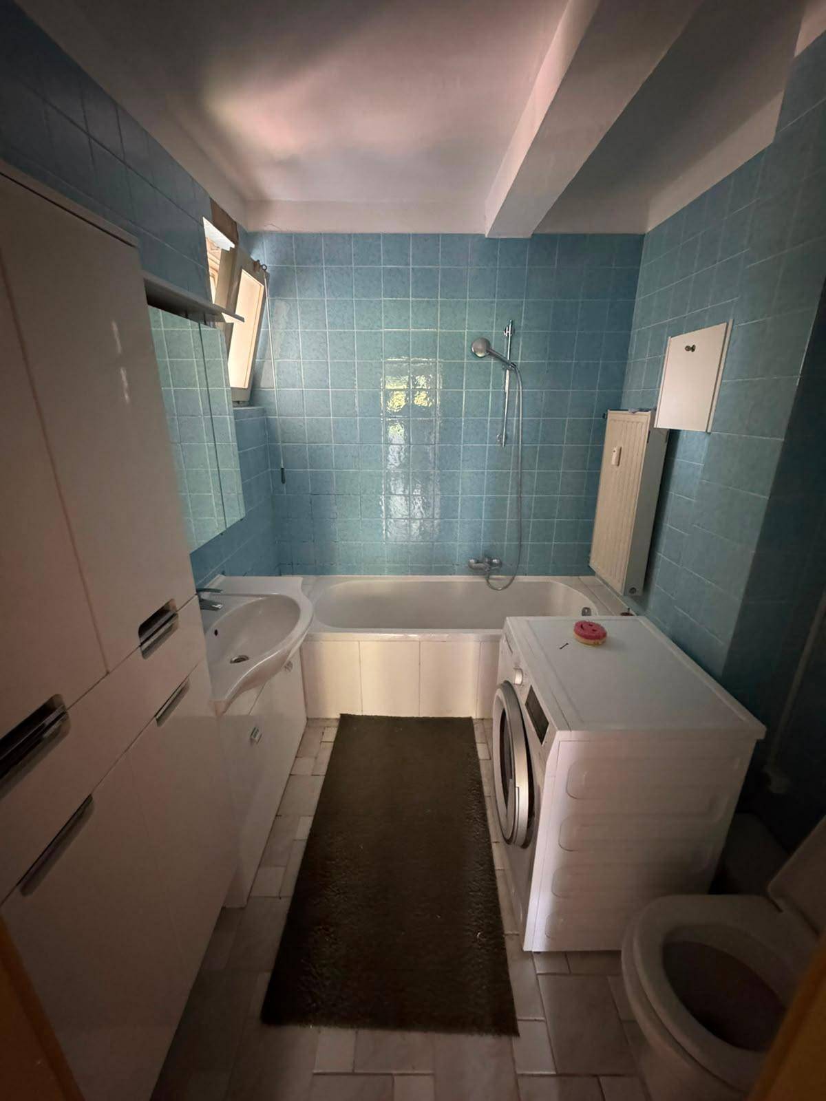 Badezimmer mit blauen Fliesen, Badewanne, Waschbecken und Waschmaschine, älterer Zustand.